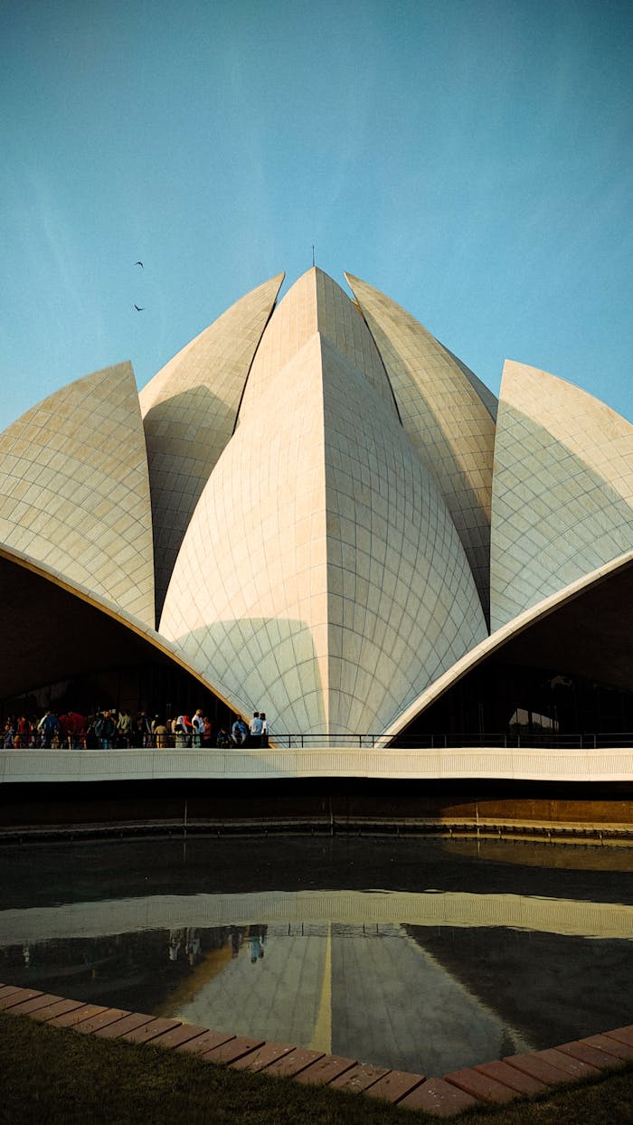 gallery-3 A breathtaking view of the Lotus Temple in New Delhi with its reflection in a pond, under a clear blue sky.